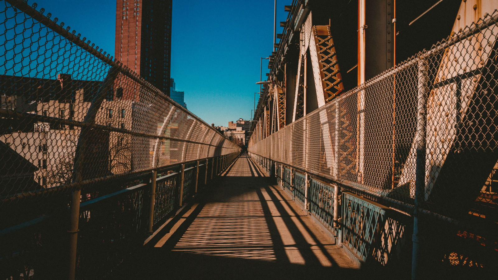 sky, wood, fence, line, suspension bridge, bridge, symmetry, canopy walkway, city, landmark, metropolitan area, tower block, building, electricity, urban area, metropolis, girder bridge, metal, pattern, cable stayed bridge, electric blue, cityscape, road, reflection, walkway, pedestrian, handrail, nonbuilding structure, steel, shadow, darkness, fixed link, guard rail, tree, night, chain link fencing, boardwalk, overpass, street, brickwork, evening, extradosed bridge, road surface, downtown, beam bridge, Brick