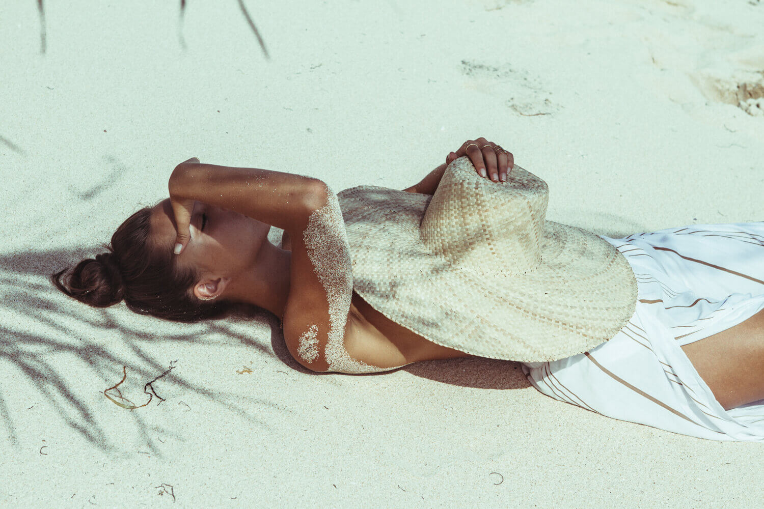 ženy, model, hairbun, bruneta, pláž, čepice, sukně, bílá sukně, písek, Přirozené světlo, ženy venku, ležící na zádech, lying on beach, women on beach, kroužky, slunečnímu záření, stín, touching face, tenký, covering boobs