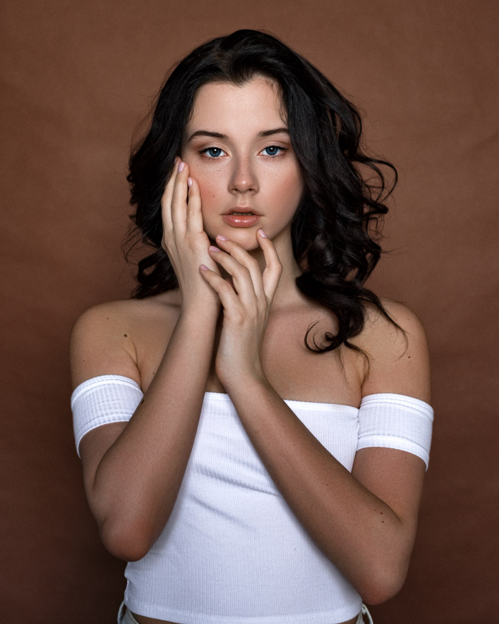 Daria Delishes, ženy, model, bruneta, modré oči, při pohledu na diváka, hnědé pozadí, uvnitř, typografické portréty, Bílé vrcholy, holá ramena, touching face, Ženy uvnitř, Max Pyzhik